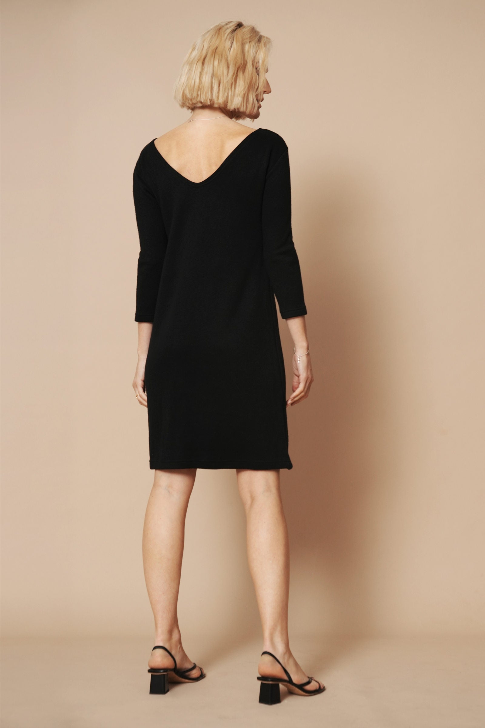 Strickkleid mit rückenausschnitt in schwarz wird von einem blonden Model getragen. Sie zeigt das schöne Kleid von hinten.