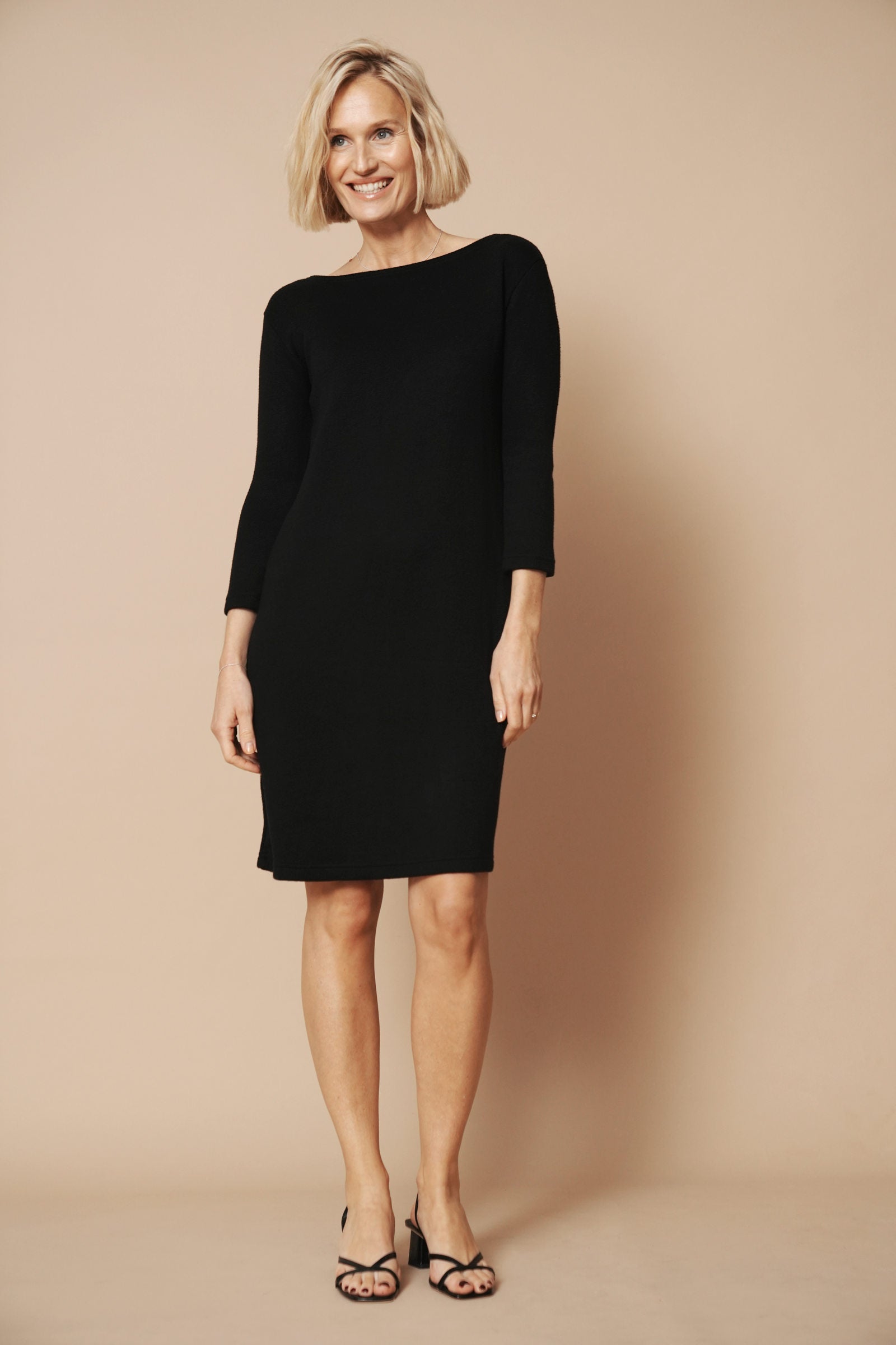 Strickkleid mit rückenausschnitt in schwarz wird von einem blonden Model getragen. Sie zeigt das schöne Kleid von vorne.