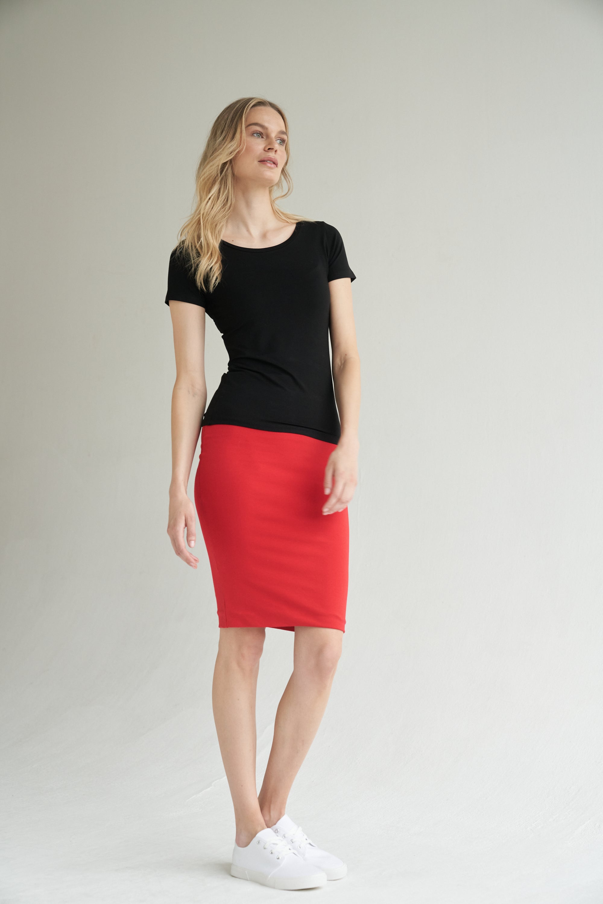 Unser Model trägt einen Bleistiftrock in rot und ein Shirt in schwarz von Bellasor. Der Bleistiftrock ist knielang. Das Model hat blondes Haar und zeigt die Ansicht von der Seite.