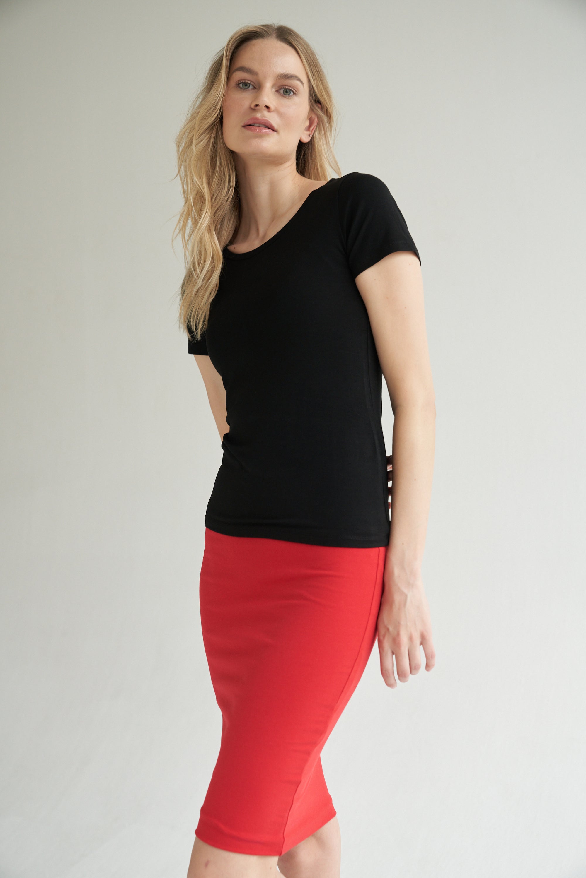 Unser Model trägt einen Bleistiftrock in rot und ein Shirt in schwarz von Bellasor. Der Bleistiftrock ist knielang. Das Model hat blondes Haar und zeigt die Ansicht von vorne.