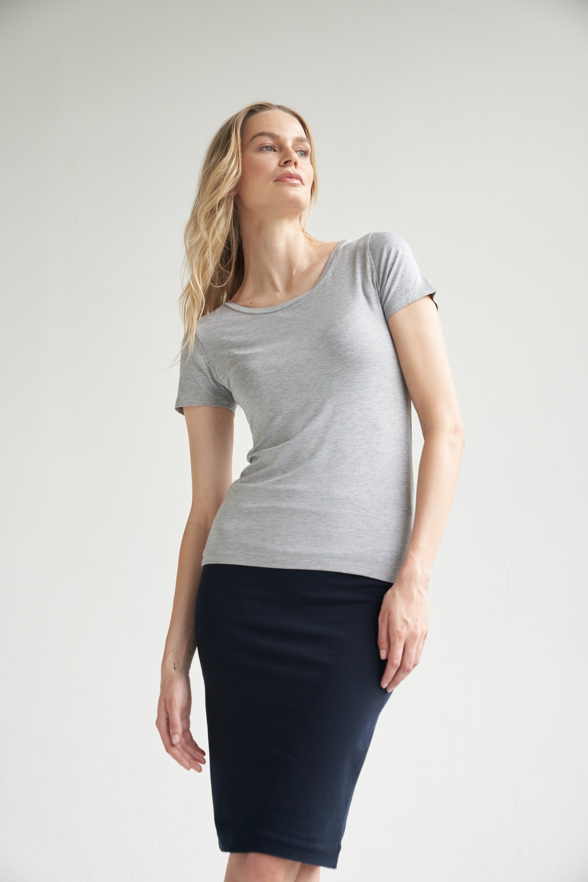 Graues T-Shirt kombiniert mit einem dunkelblauen Bleistiftrock wird von einem blonden Model getragen.  