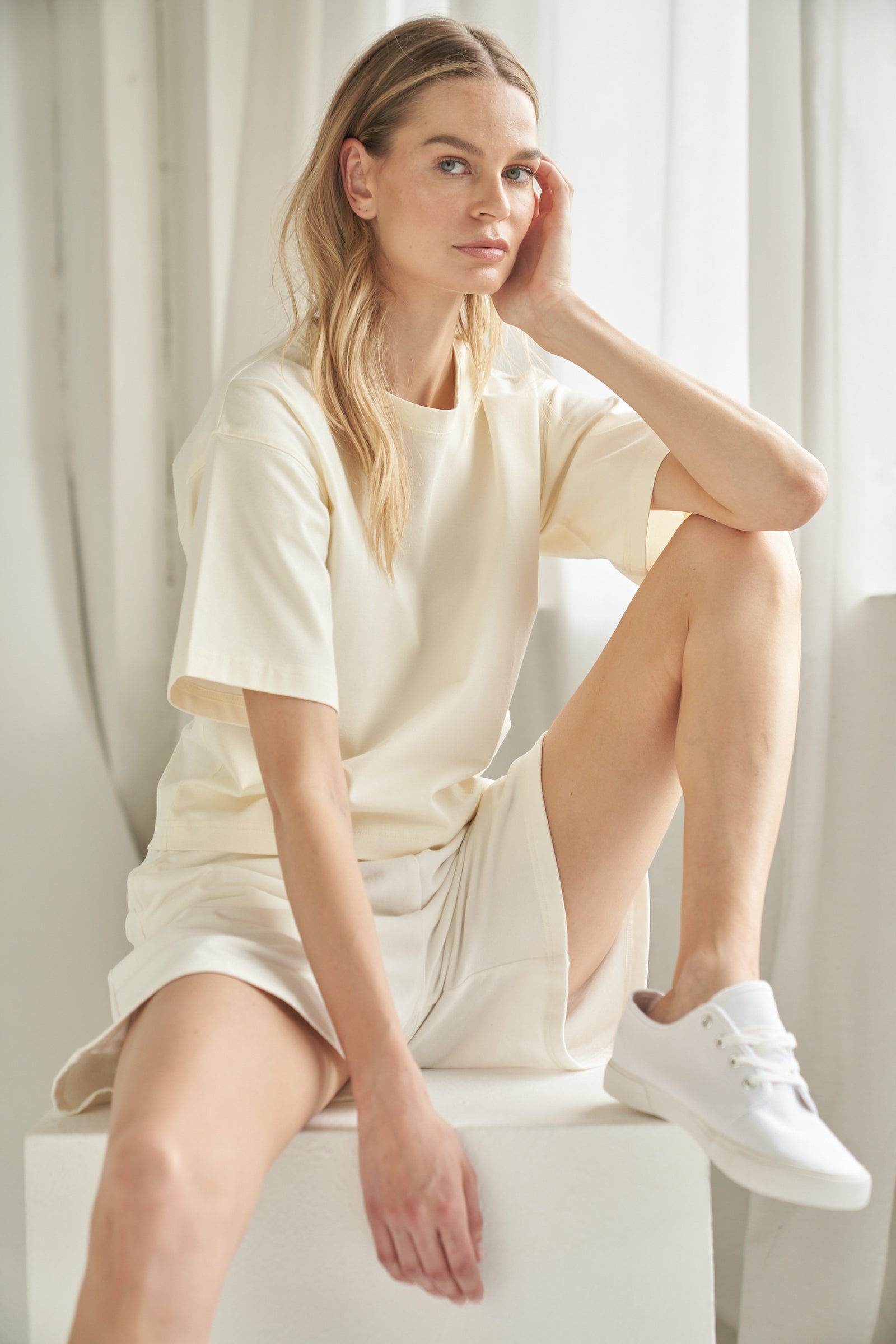 T-shirt aus Bio-Baumwolle in der Farbe cremeweiss. Das T-Shirt wird von einem blonden Model in sitzender Haltung getragen und zeigt das Outfit von vorne.