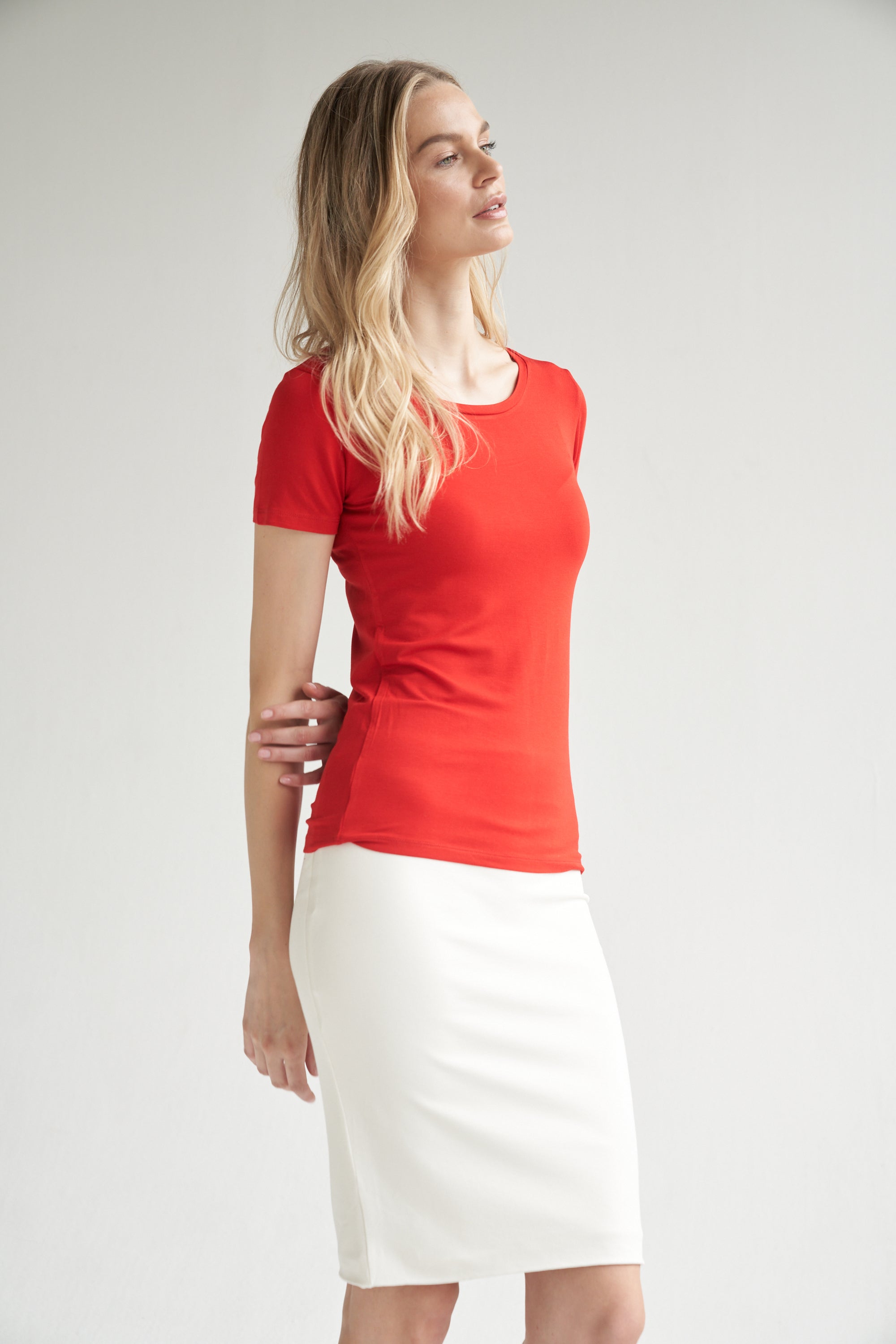 Unser Model trägt einen Bleistiftrock in weiß und ein Shirt in rot von Bellasor. Der Bleistiftrock ist knielang. Das Model hat blondes Haar und zeigt die Ansicht von der Seite.