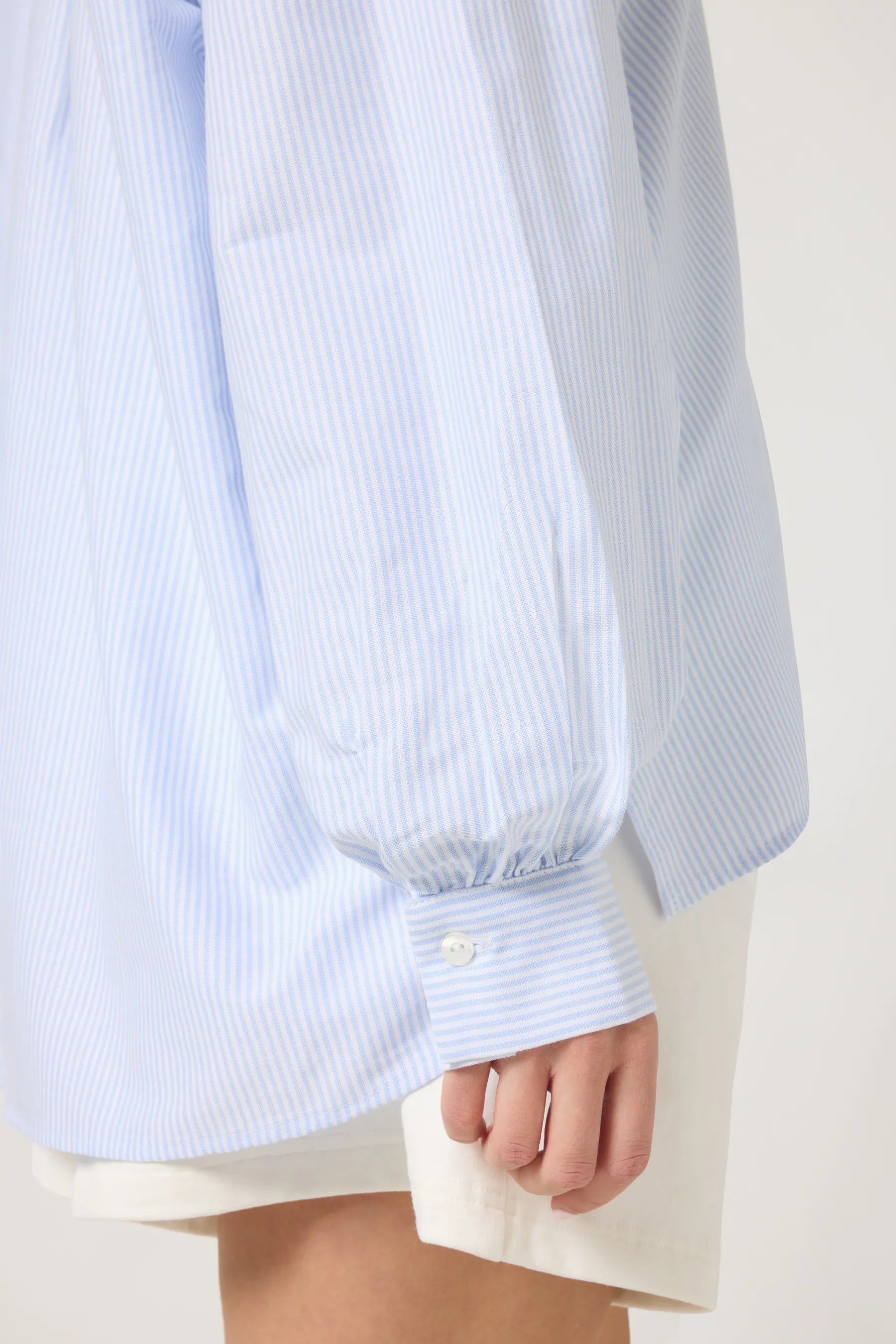 Detailansich der hellblauen, gestreiften Oversize-Bluse für Damen, getragen von einem weiblichen Model im Studio vor einer cappuccino-farbenen Wand.