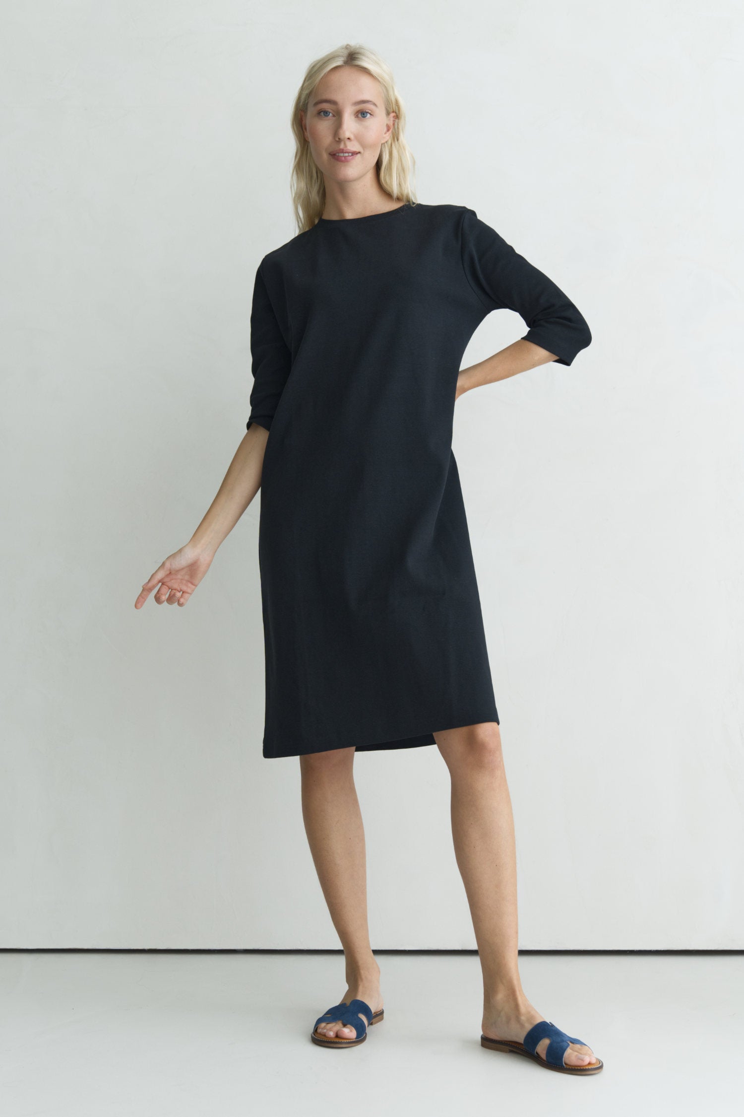 Model in einem schwarzen Shirtkleid vor einer Wand.