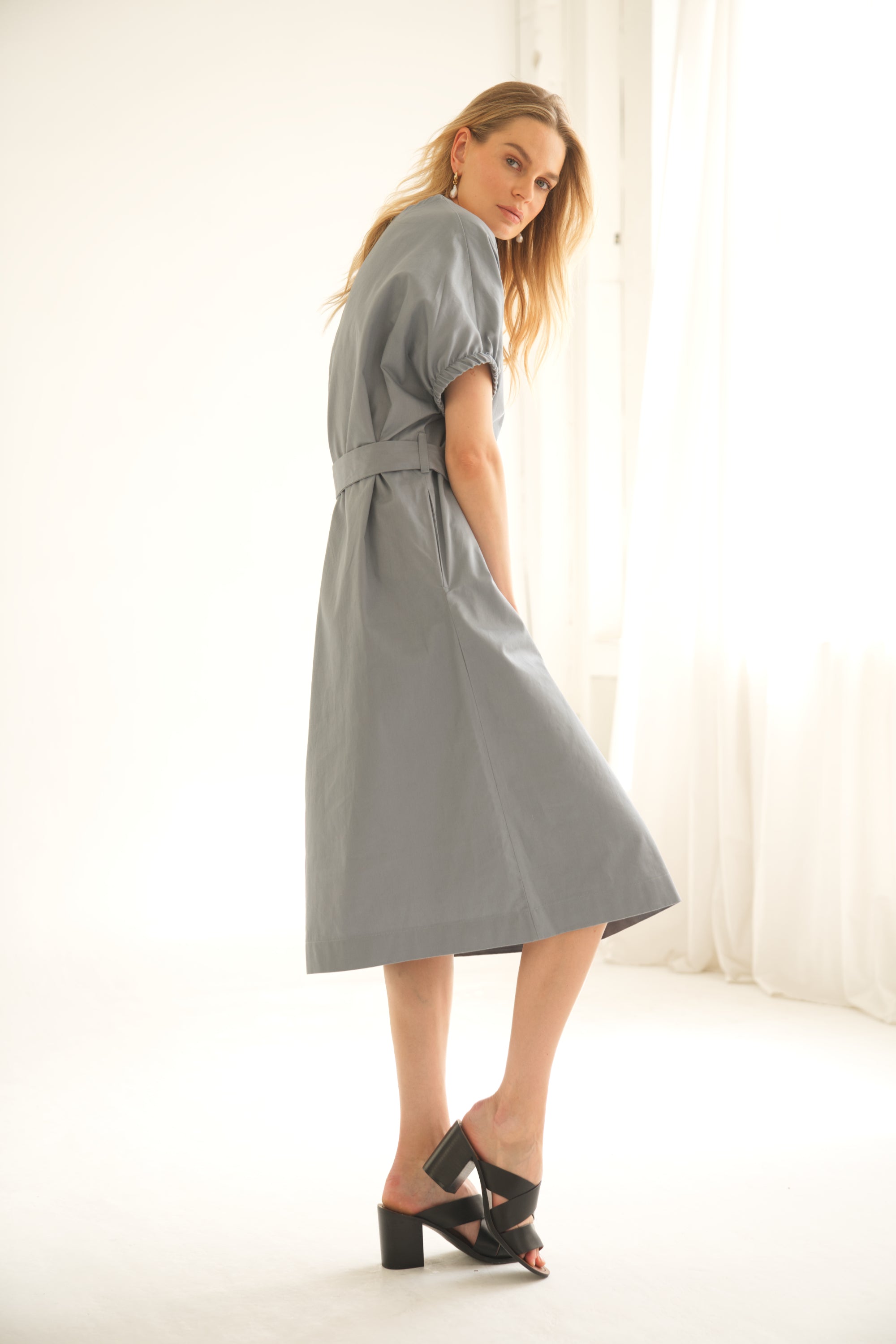 Oversize-Kleid aus Baumwolle in der Farbe blau wird von einem blonden Model getragen. Sie zeigt sich von der Seite.