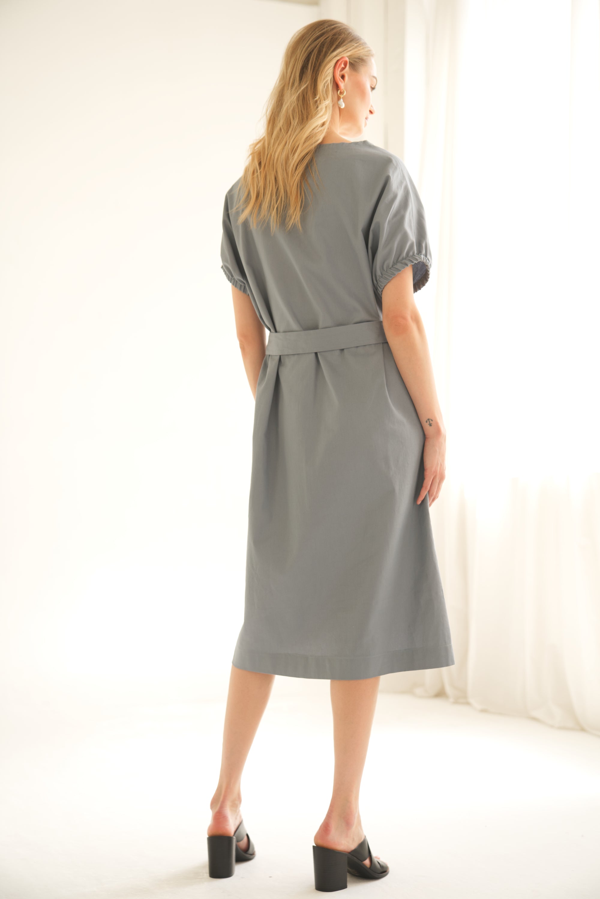 Oversize-Kleid aus Baumwolle in der Farbe blau wird von einem blonden Model getragen. Das Model wird von hinten gezeigt.