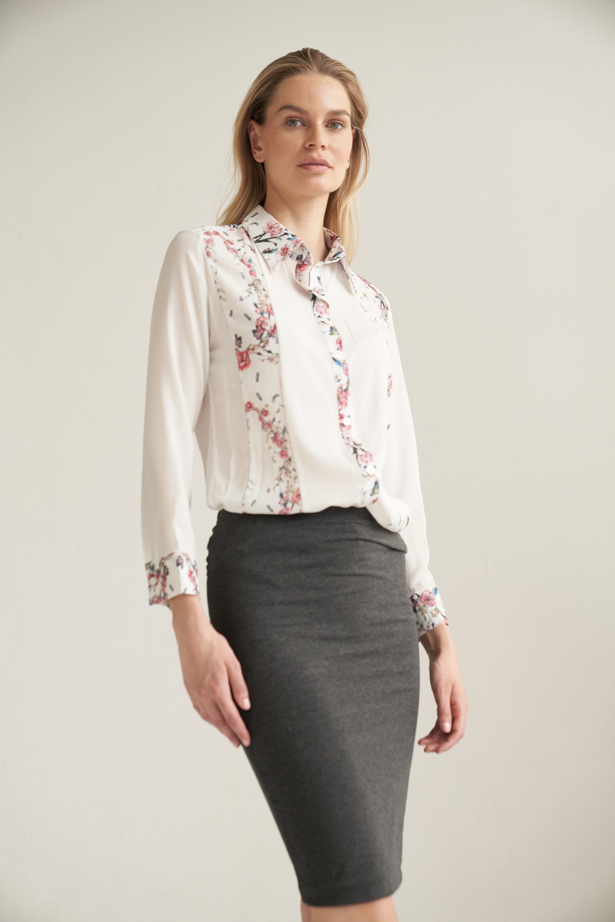 Weisse Bluse mit Blumenmuster kombiniert mit einem Bleistiftrock in dunkelgrau. Das Outfit wird von einem blonden Model getragen.