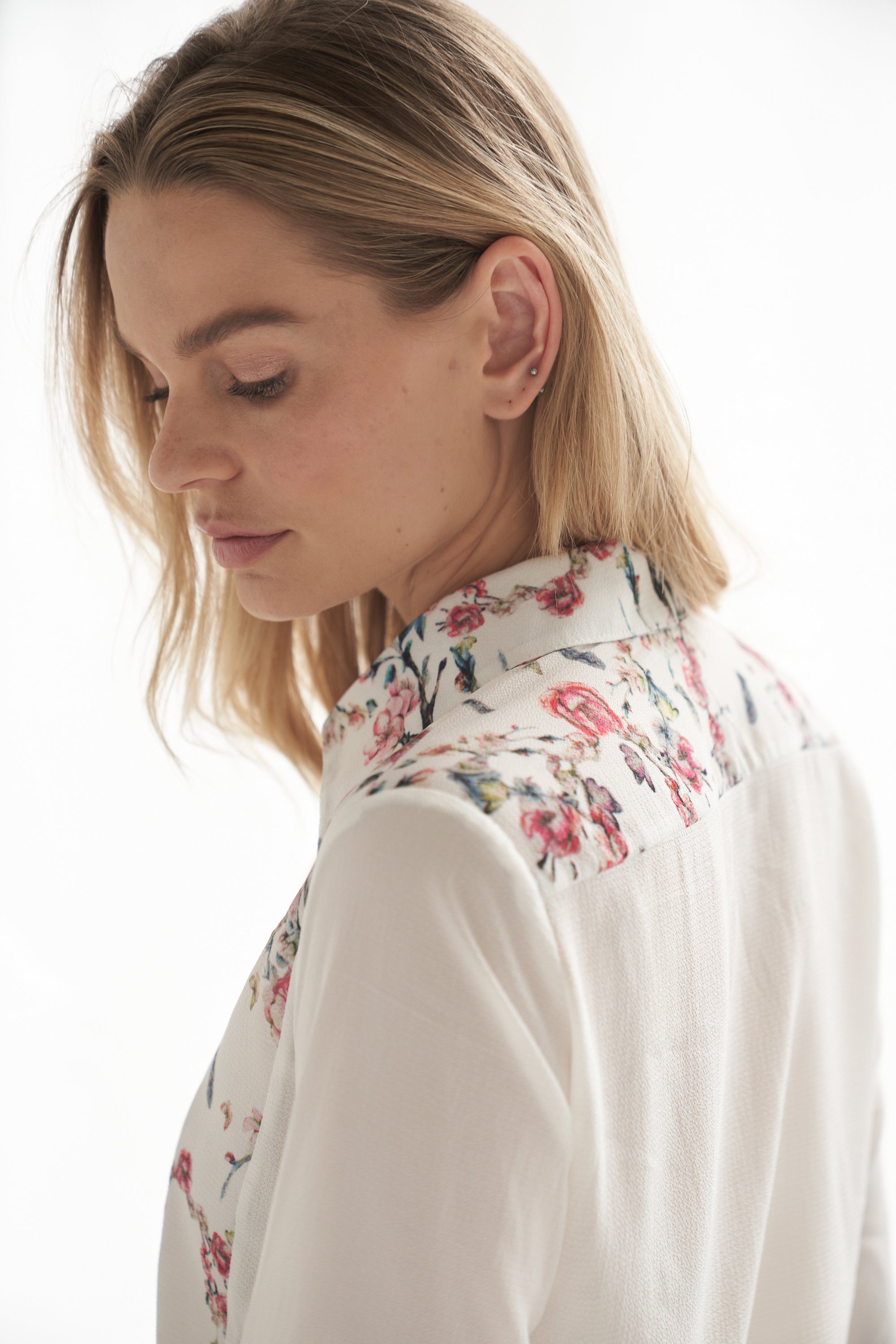 Detailansicht von einer weissen Bluse mit Blumenmuster. Die Bluse wird von einem blonden Model getragen.