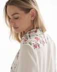 Detailansicht von einer weissen Bluse mit Blumenmuster. Die Bluse wird von einem blonden Model getragen.